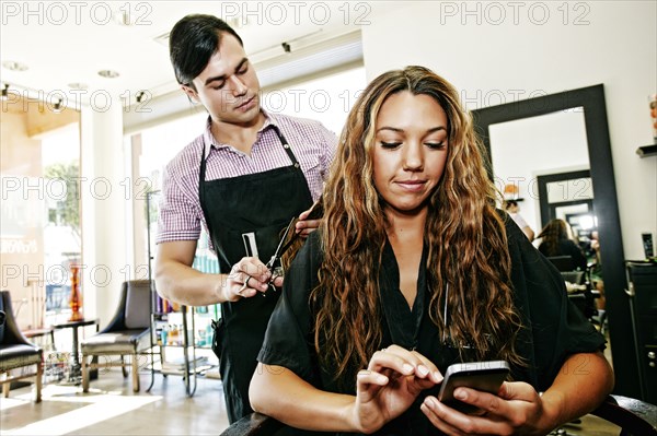 Hairdresser with customer texting on cell phone in hair salon