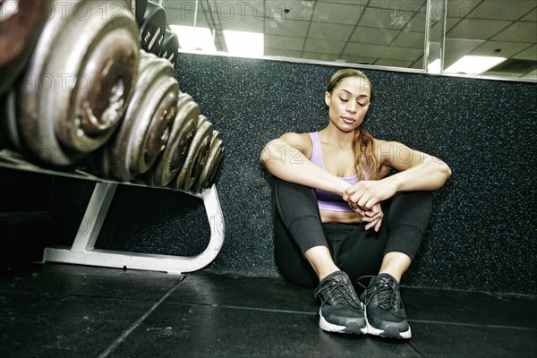 Mixed Race woman sitting on floor resting in gymnasium