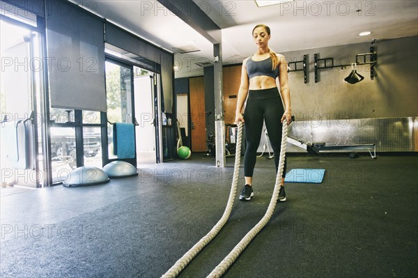 Mixed Race woman working out with heavy ropes in gymnasium