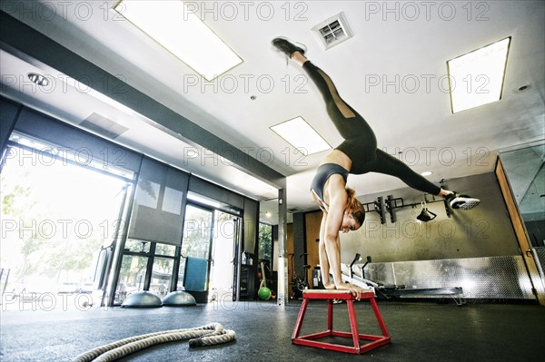 Mixed Race woman doing handstand on stool in gymnasium