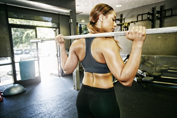 Mixed Race woman stretching with barbell in gymnasium