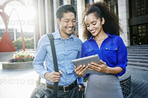 Smiling business people using digital tablet in plaza outdoors