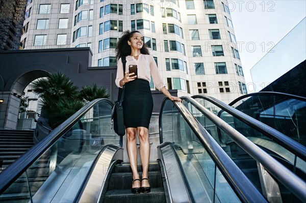 Smiling Hispanic businesswoman riding escalator outdoors