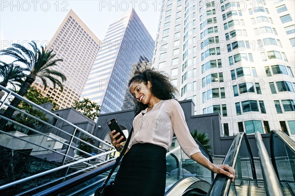 Smiling Hispanic businesswoman texting on escalator outdoors