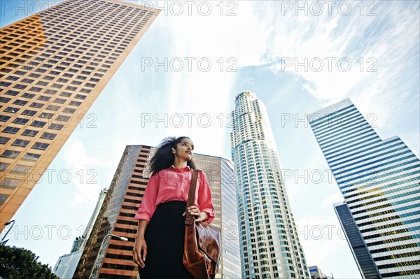 Serious Hispanic businesswoman near highrises in city