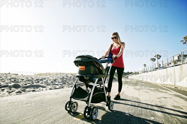 Mother pushing baby son in stroller at beach