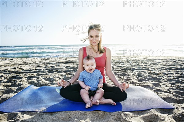 Smiling mother doing yoga at beach with baby son