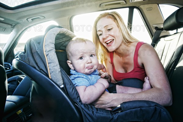 Mother buckling pouting baby son in car seat