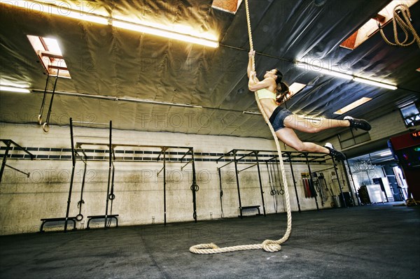 Mixed Race woman climbing rope in gymnasium