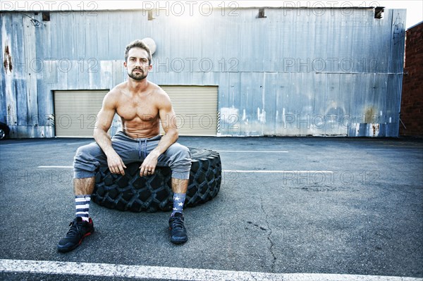 Caucasian man sitting on heavy tire outdoors