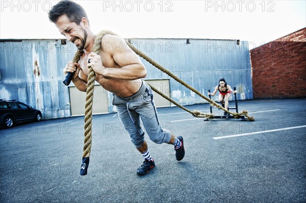 Caucasian man pulling woman with heavy ropes in parking lot outdoors