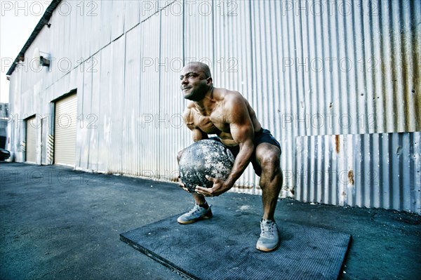 Black man lifting heavy ball outdoors