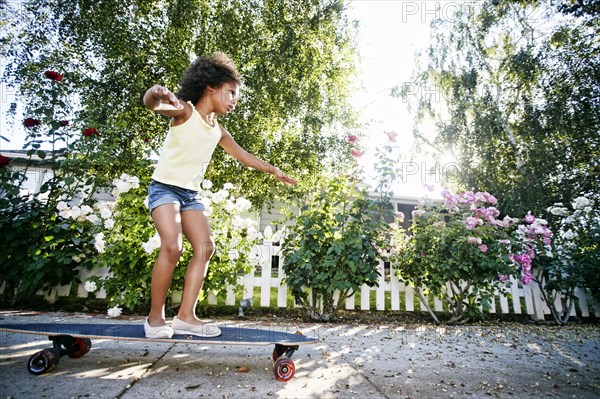 Mixed Race girl skateboarding on sidewalk