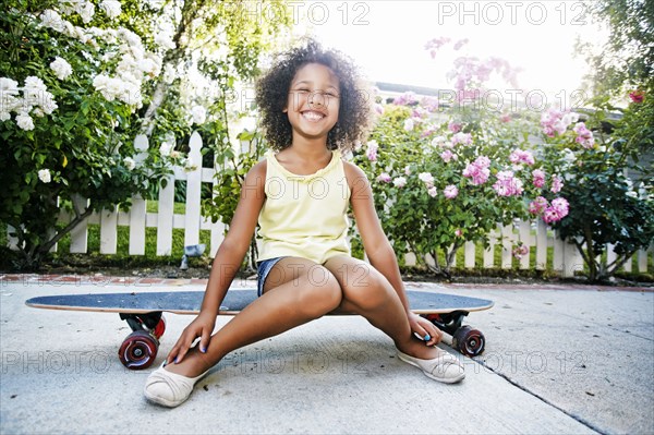 Smiling Mixed Race girl sitting on skateboard
