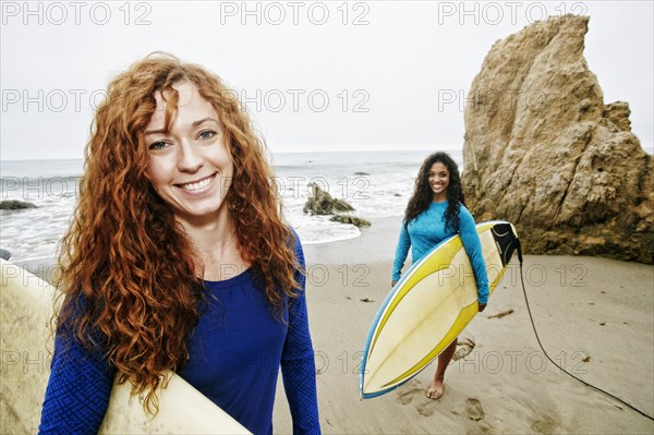 Smiling women holding surfboards at beach