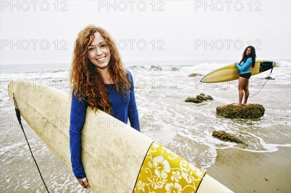 Smiling women holding surfboards at beach