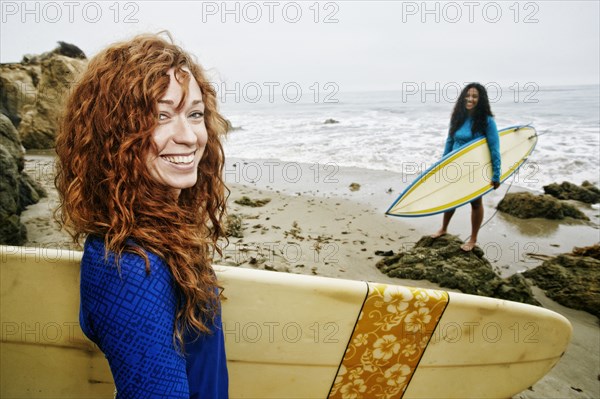 Smiling women holding surfboards at beach