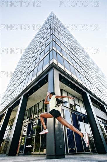 Black woman running and jumping on city sidewalk