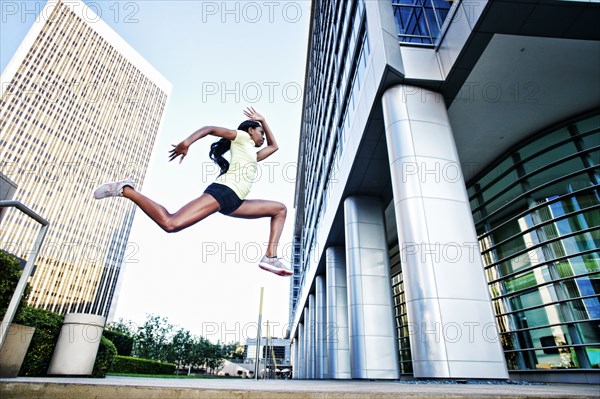 Black woman running and jumping on city sidewalk