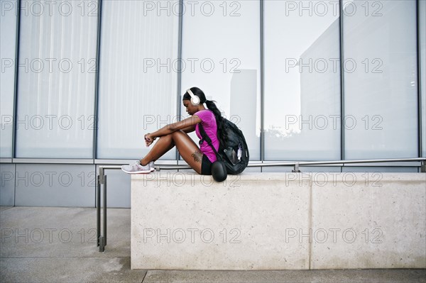 Black woman sitting on urban wall listening to headphones