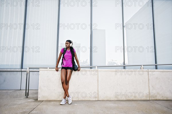 Black woman leaning on urban wall listening to headphones