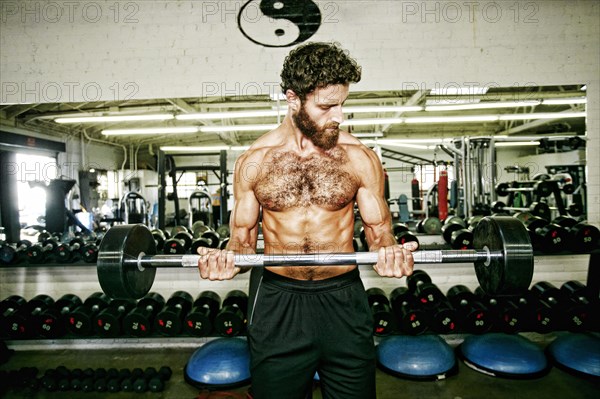 Mixed Race man lifting barbell in gymnasium