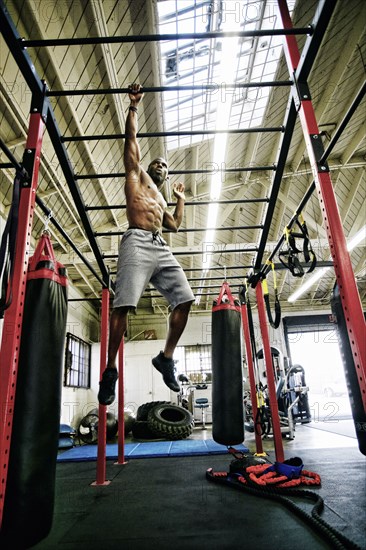 Black man hanging from bars in gymnasium