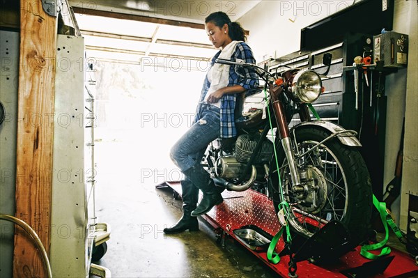 Mixed Race woman leaning on motorcycle in garage