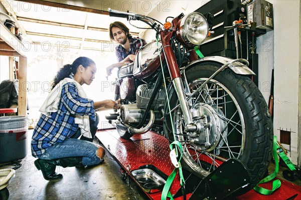 Man watching woman repairing motorcycle in garage