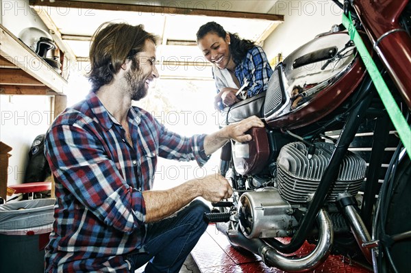 Woman watching man repairing motorcycle in garage