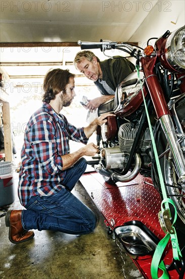 Caucasian father watching son repairing motorcycle in garage