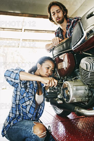 Man watching woman repairing motorcycle in garage