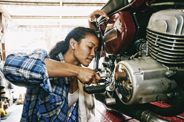 Mixed Race woman repairing motorcycle in garage