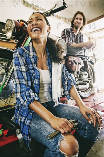 Laughing man and woman repairing motorcycle in garage