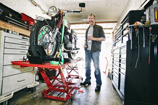 Caucasian man drinking coffee while repairing motorcycle in garage