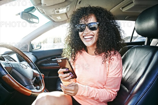 Laughing Hispanic woman in car holding texting on cell phone