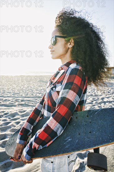 Hispanic woman holding skateboard at beach