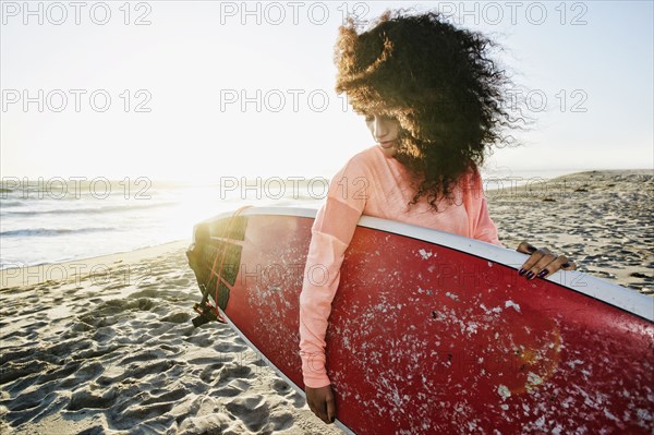 Hispanic woman holding surfboard at beach