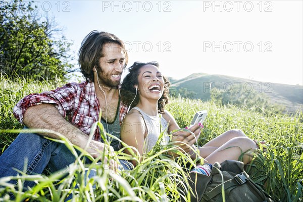Smiling couple sitting on hill listening to cell phone
