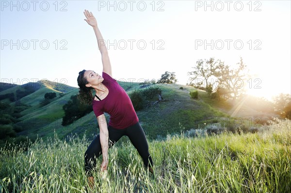 Mixed Race woman practicing yoga on hill