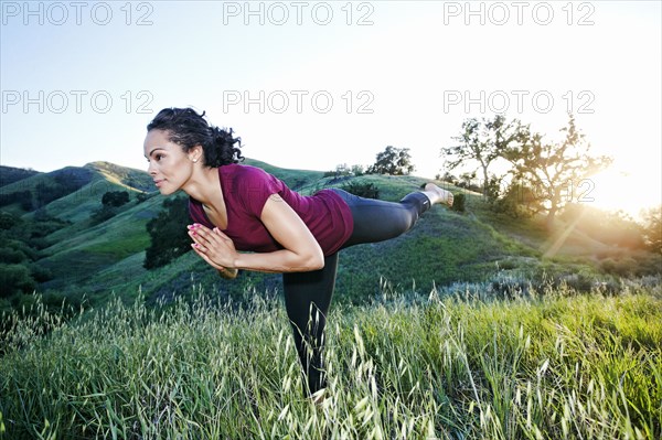 Mixed Race woman practicing yoga on hill