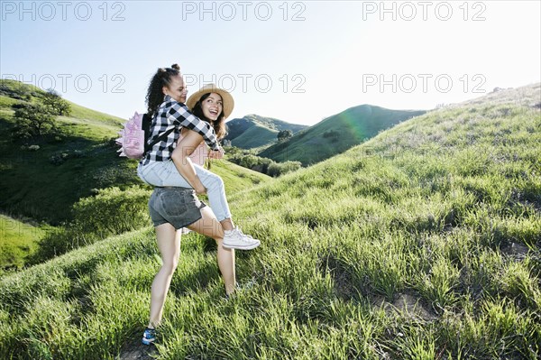 Mother carrying daughter piggyback on hill