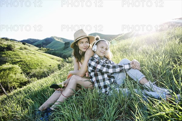 Mother and daughter sitting on hill listening to headphones