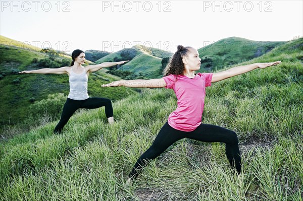 Mother and daughter practicing yoga on hill