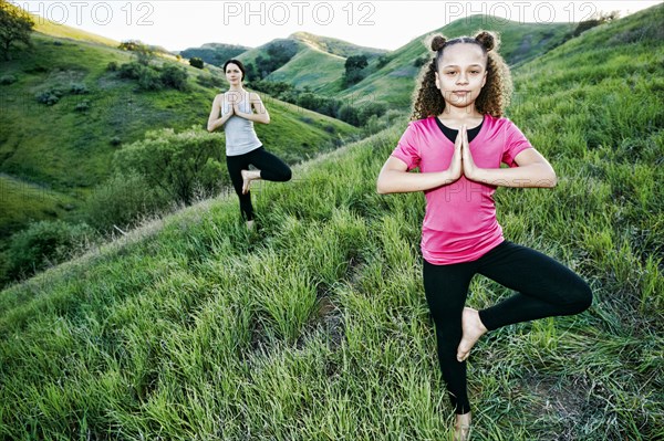 Mother and daughter practicing yoga on hill