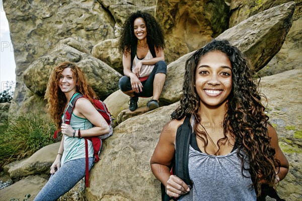 Smiling women carrying backpacks near rock formation