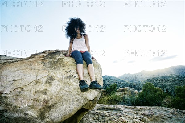 Hispanic woman sitting on boulder in wind