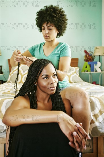 Woman braiding hair of friend in bedroom