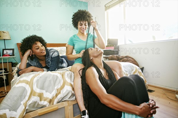 Woman braiding hair of friend in bedroom