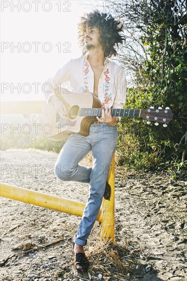 Mixed Race man leaning on gate playing guitar